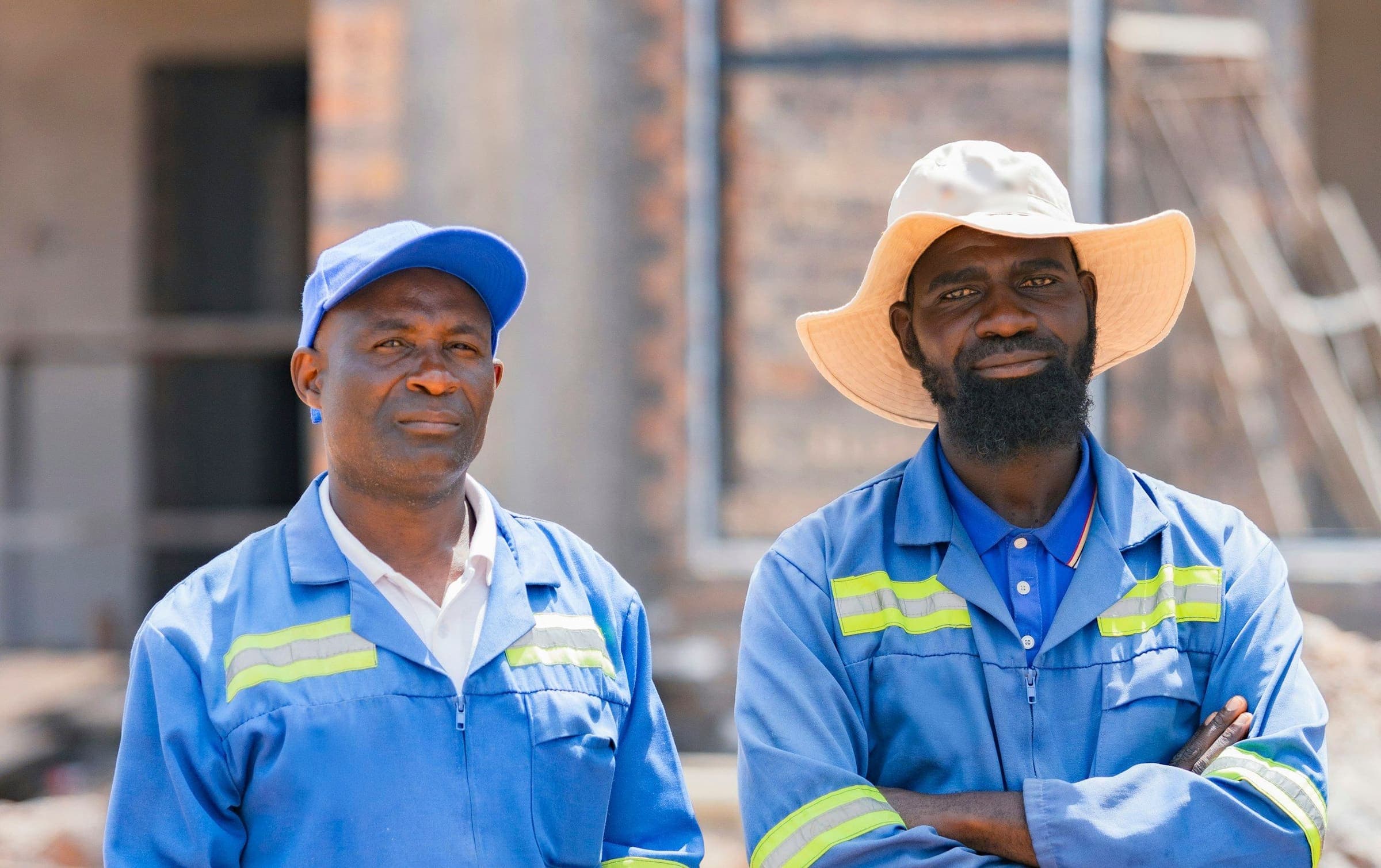 Two experienced site workers in blue overalls in front of a building under construction.