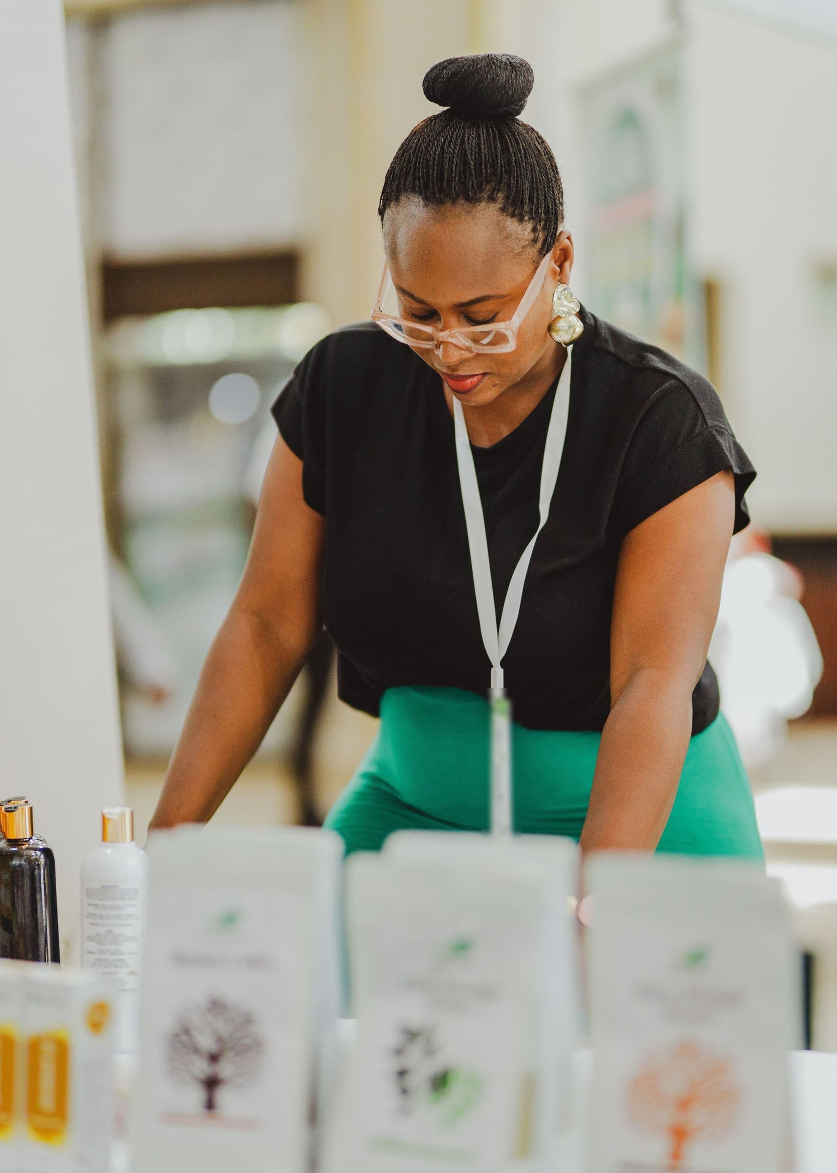 A businesswoman wearing a delegate lanyard arranges product samples on an exhibition table.